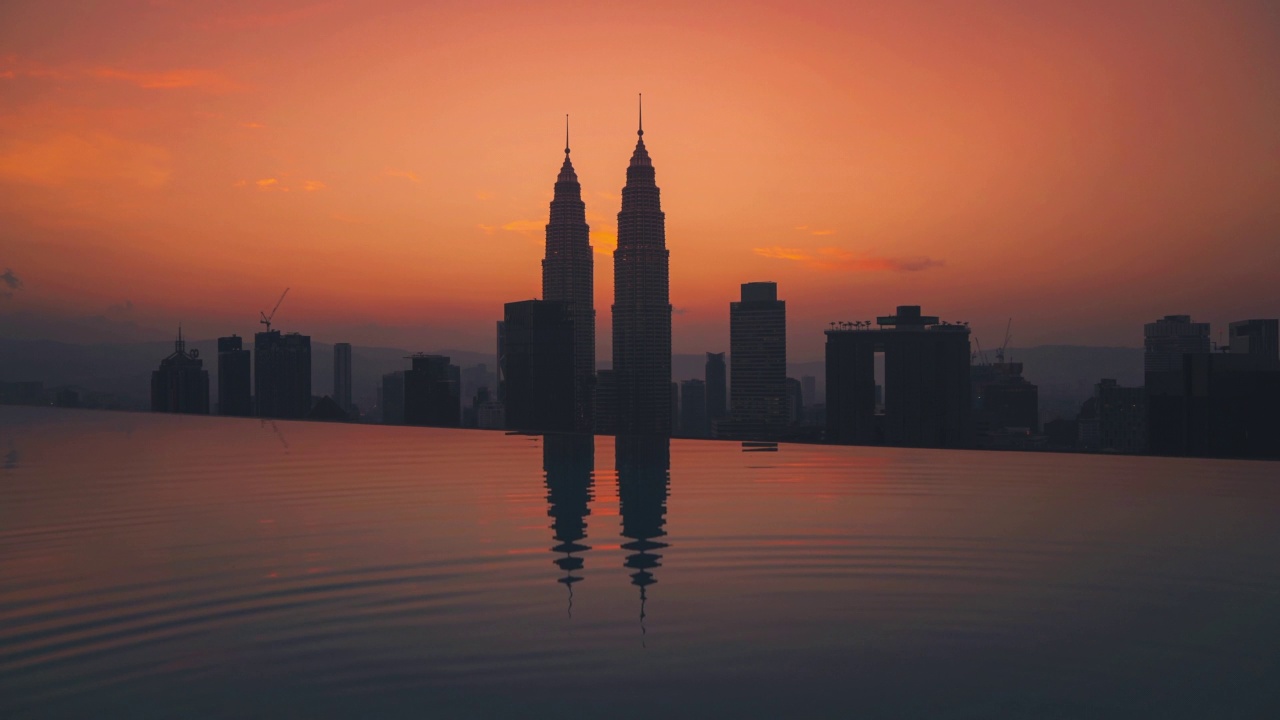 吉隆坡早晨日出的Cinemagraph，俯瞰城市，在日出时面对标志性的双子塔，前景是一个无边无际的屋顶游泳池。马来西亚的豪华旅游酒店。4K超高清动态画面无缝视频循环。视频下载
