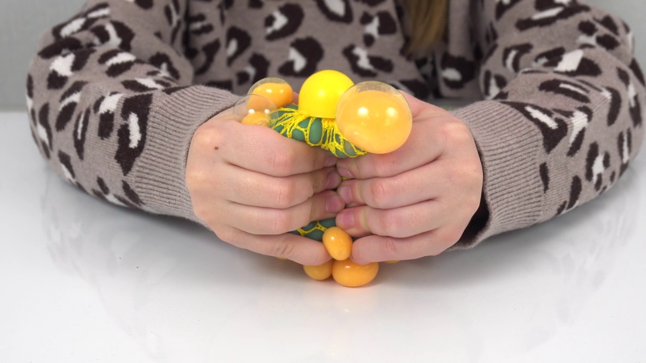 孩子的手在白色上挤压压力球。小女孩挤压绿色和黄色的抗压力玩具。视频下载