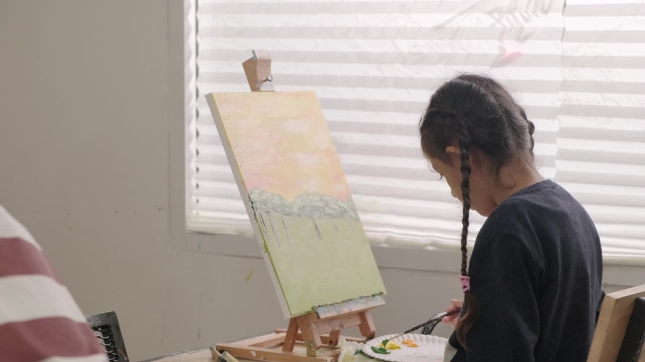 在美术教室里，一个小女孩正专注地在画布上画亚克力彩画。视频素材