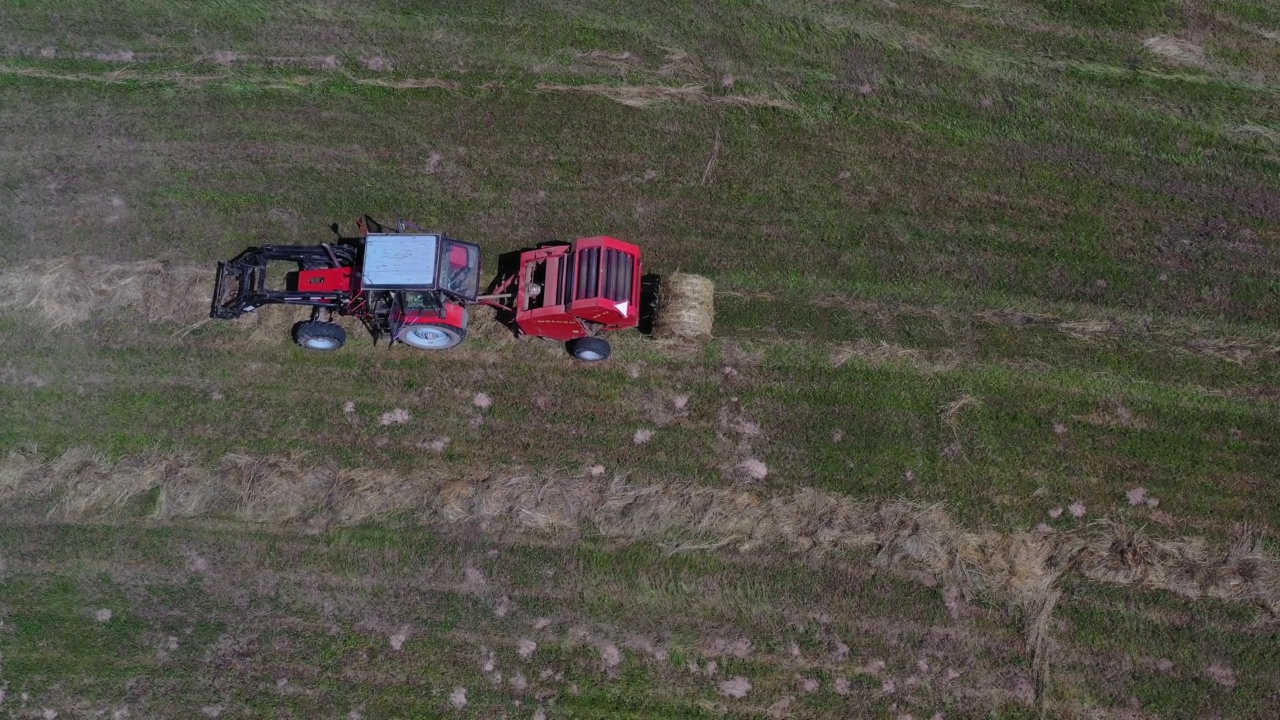 拖拉机使用拖捆机从草地上收集干草，并制成卷，空运视频下载