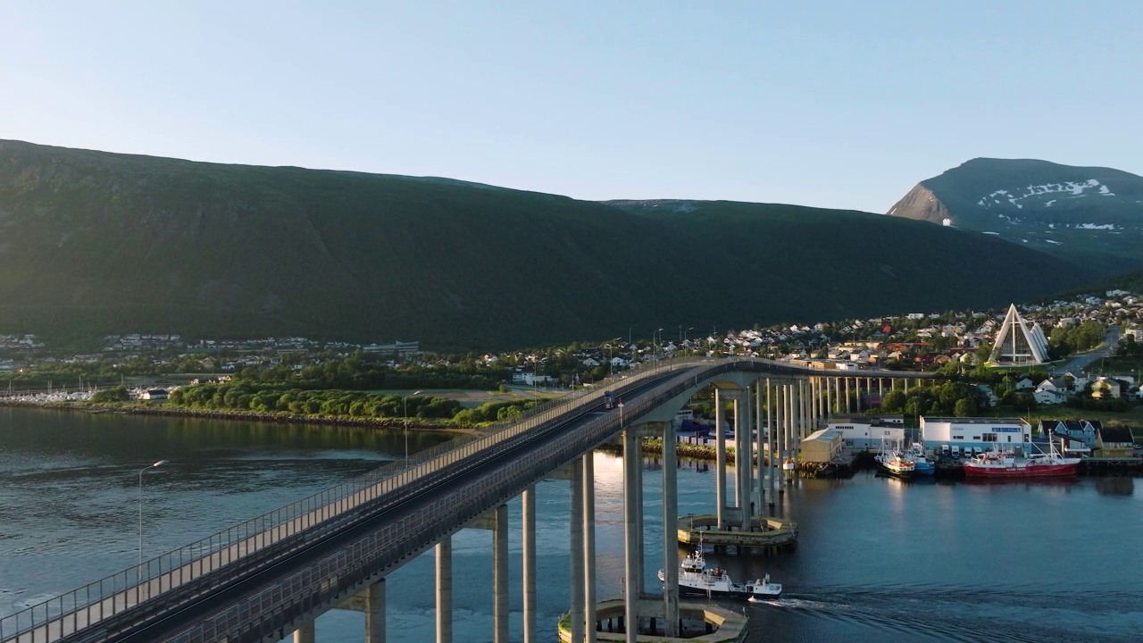 在挪威特罗姆瑟的城市背景上，一座桥和大海的航拍慢镜头，还有一艘穿越的船视频下载