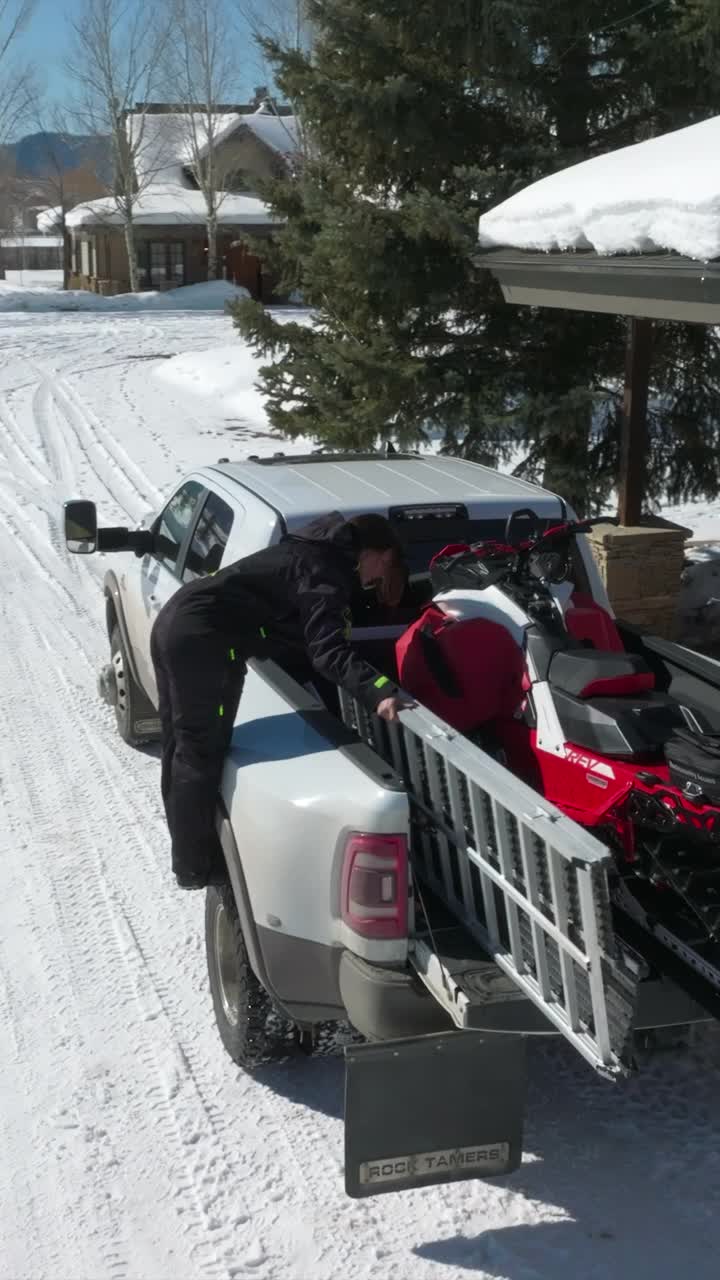 一名女子正在装载一辆小型卡车，空中无人机正在观察山上雪地上的摩托雪橇。-垂直格式-延时视频下载