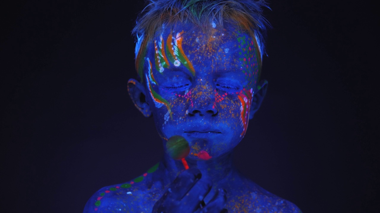 在荧光灯的照射下，一个男孩拿着棒棒糖，画着紫外线画。视频下载