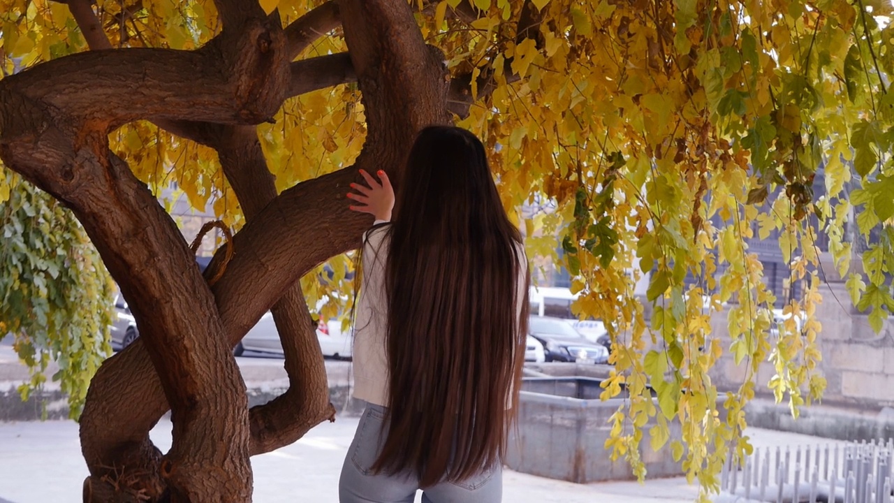 一位身穿白衬衫和牛仔裤、黑发黑发的中东年轻美女正在秋天的公园里散步，正在打电话。可爱的亚美尼亚或土耳其妇女在户外使用智能手机说话视频下载