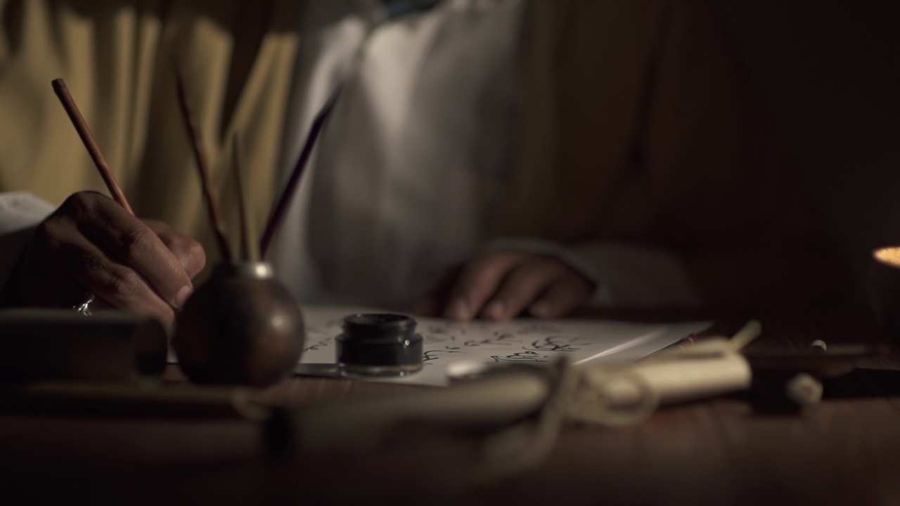 一个中世纪的人用一支有墨水的旧钢笔在蜡烛点燃的纸上写字视频下载