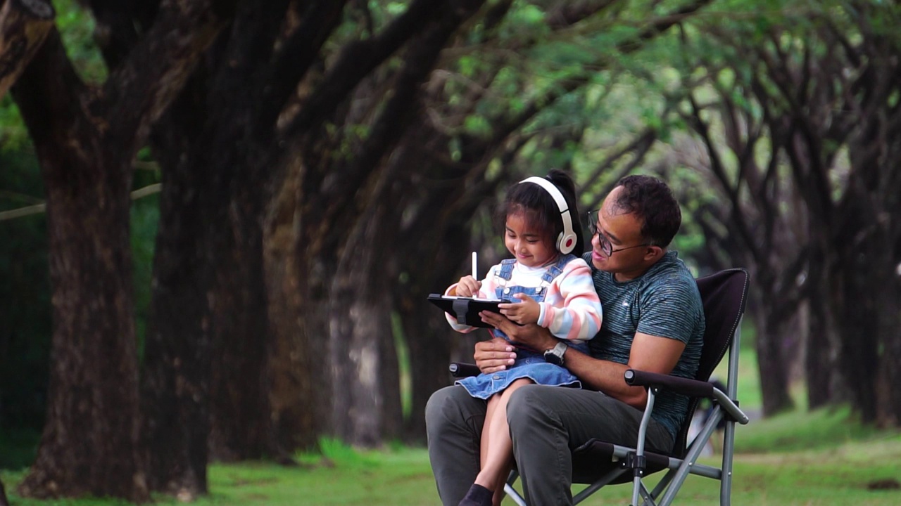 孩子们和他们的父亲在公园里快乐地坐在椅子上视频素材