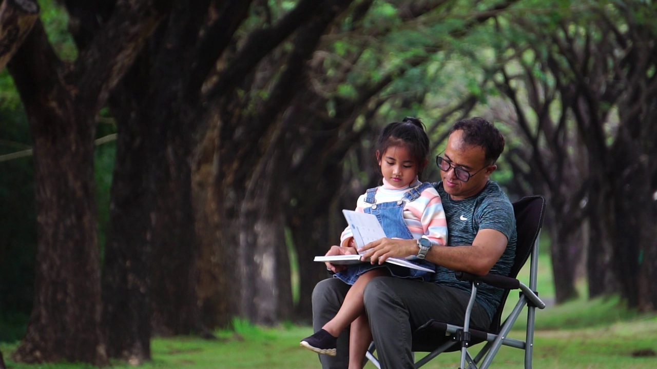 孩子们和他们的父亲在公园里快乐地坐在椅子上视频素材