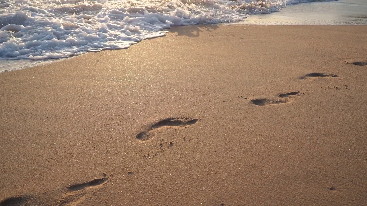 4K拍摄的泡沫海浪冲击沙滩，抹去夕阳下人类的脚印视频下载