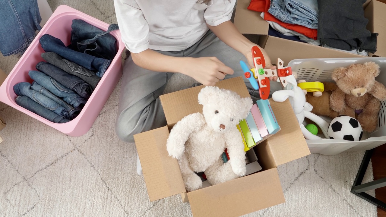 男孩为慈善捐赠准备衣服和玩具。十几岁的男孩整理和儿童玩具，衣服装在家里的盒子里。孩子们玩着旧玩具，把它们装进纸箱里视频素材