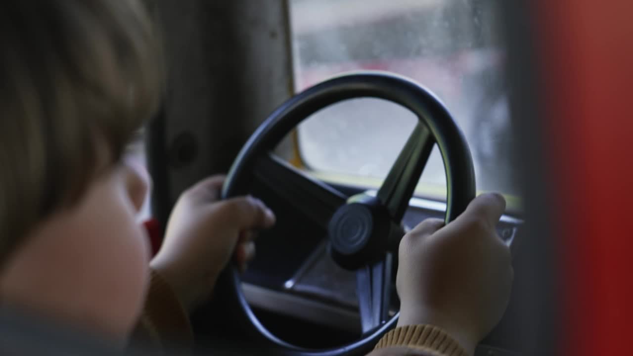 一个孩子假装在游乐园的旋转木马里开车。小男孩拿着玩具方向盘视频素材