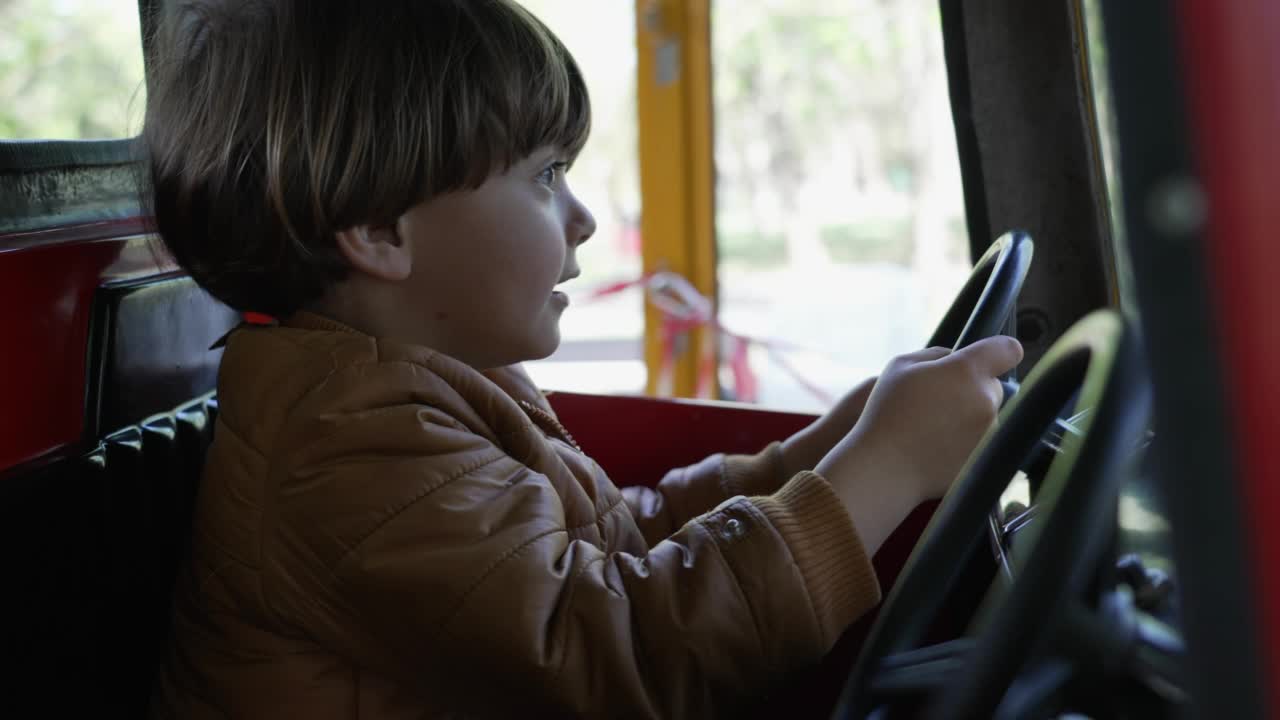 一个快乐的小男孩在游乐园的旋转木马上驾驶玩具车。孩子拿着方向盘假装开车视频素材