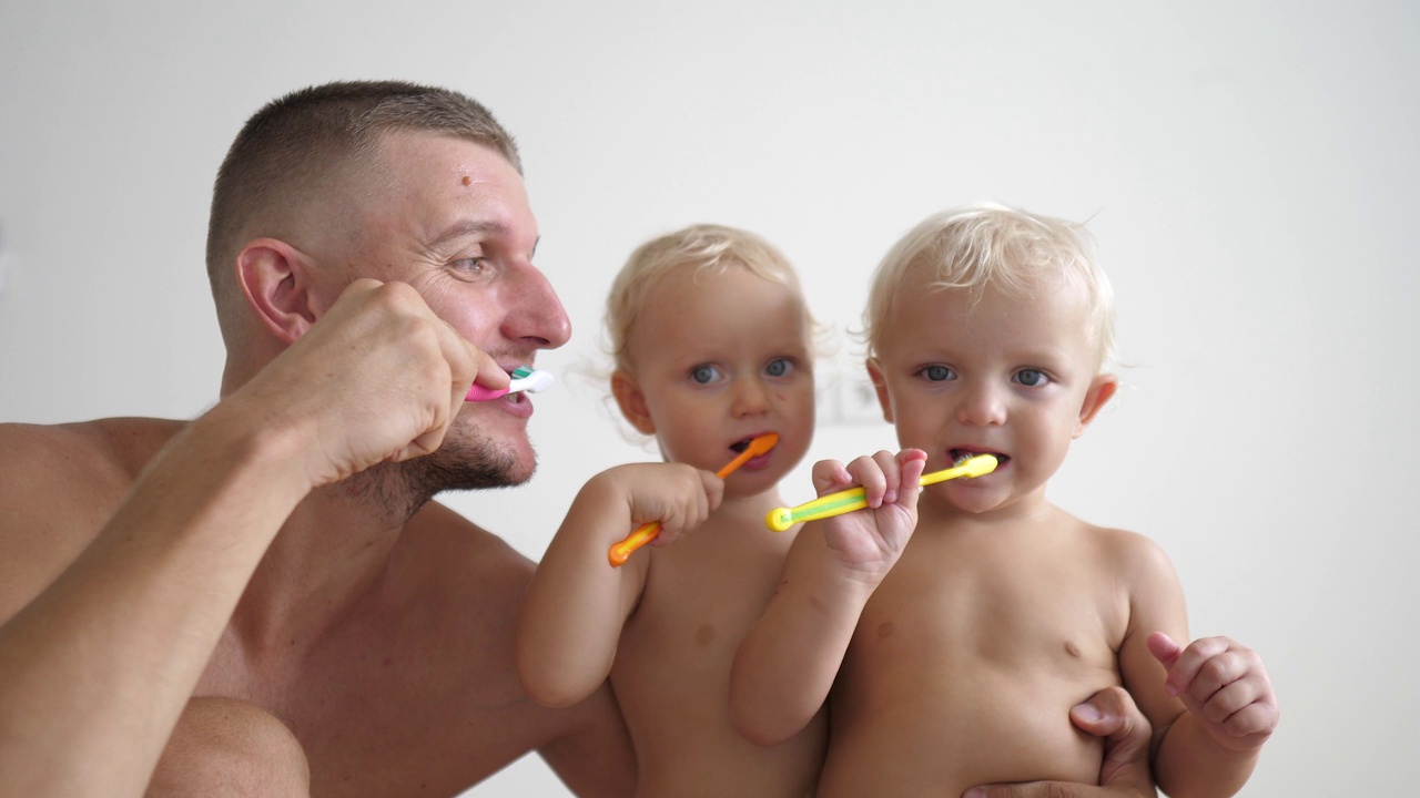 养成早晨的卫生习惯。爸爸教他的双胞胎宝宝如何刷牙。父亲给孩子树立了从小刷牙的榜样。口腔卫生的概念。视频下载