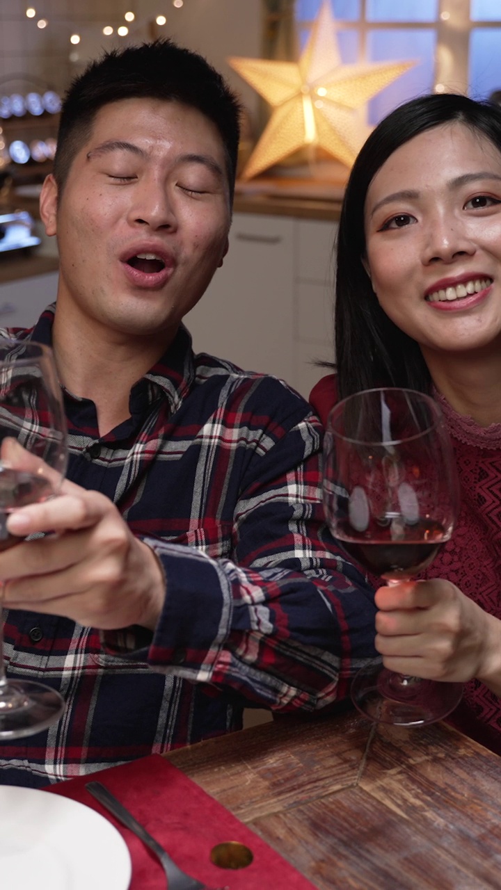 垂直屏幕:快乐的亚洲年轻夫妇看着手机摄像头，在一个舒适的家里吃饭，在虚拟聊天中向朋友敬酒。视频下载