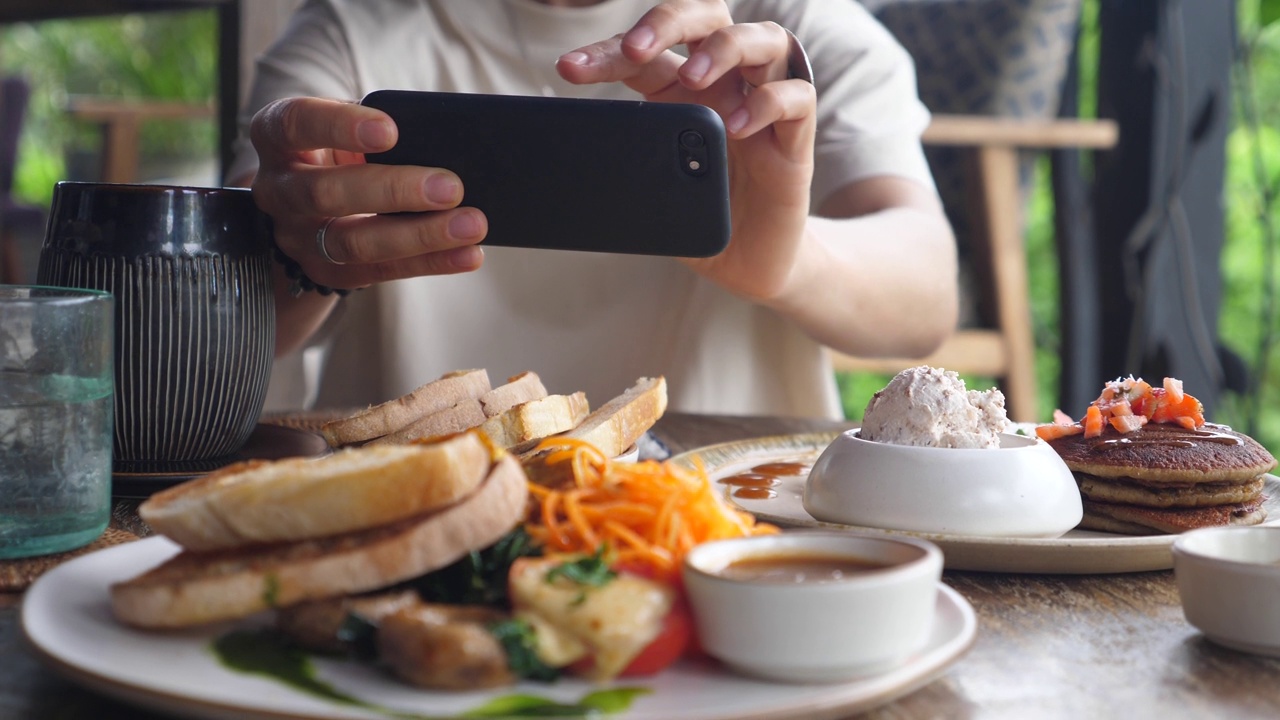 特写人类的手拍摄食物被端上木桌。素食早餐作为食物博客的内容。用手机依次拍摄每道菜。视频下载