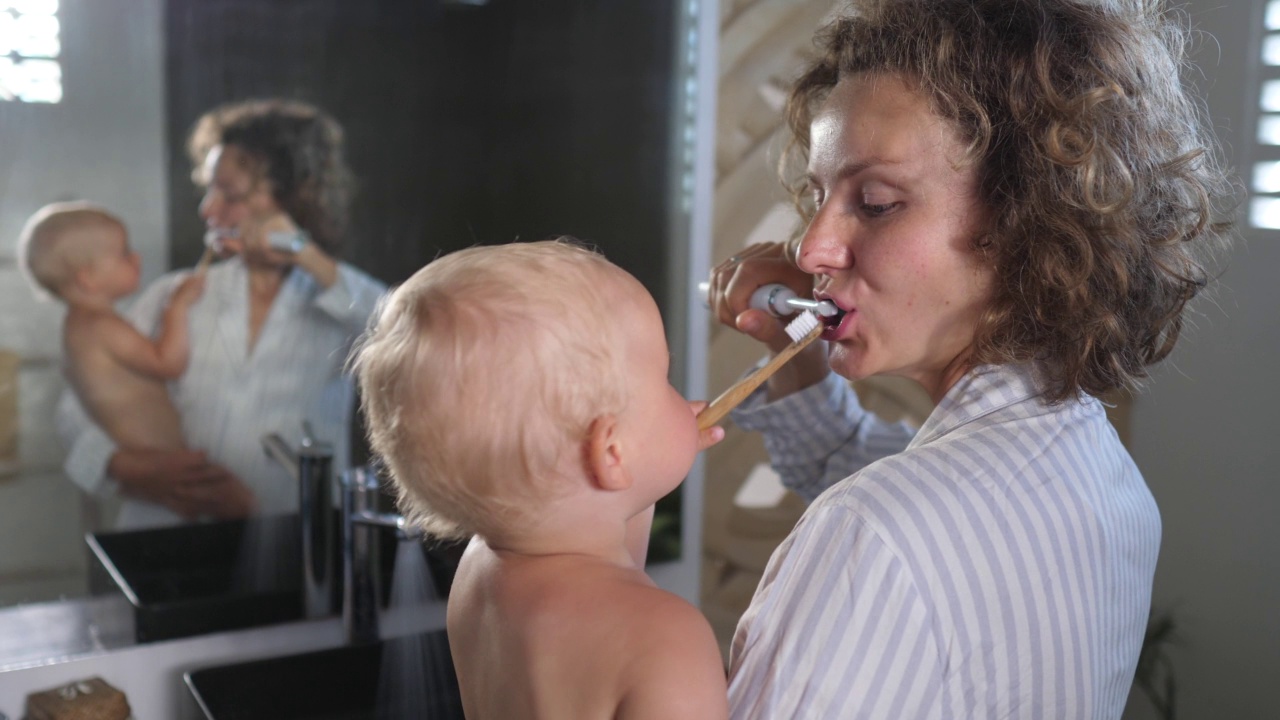 年轻的白人母亲抱着一起刷牙的孩子。他们每天都有自己的早操。他们一起刷牙很开心。视频素材