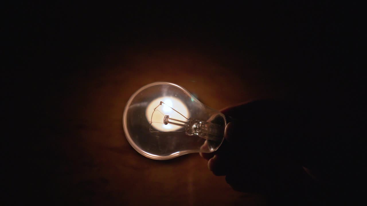 在燃烧的蜡烛的灯光下，手里拿着灯泡。特写镜头视频下载