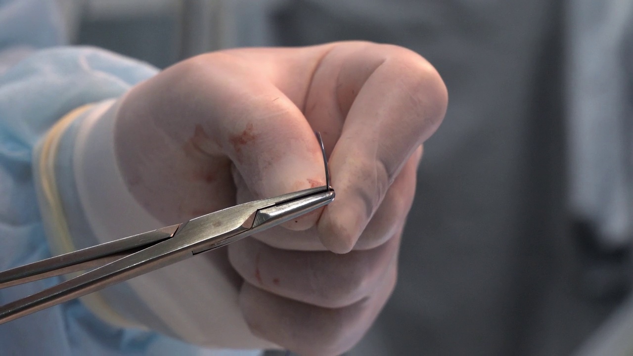 外科医生用带着血迹的医用手套的手取出针线。医生正准备缝合手术切口。概念的结束操作。视频下载