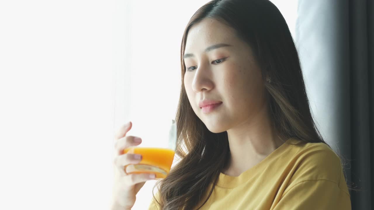 特写年轻美丽的亚洲妇女在厨房喝橙汁，健康的生活方式视频素材