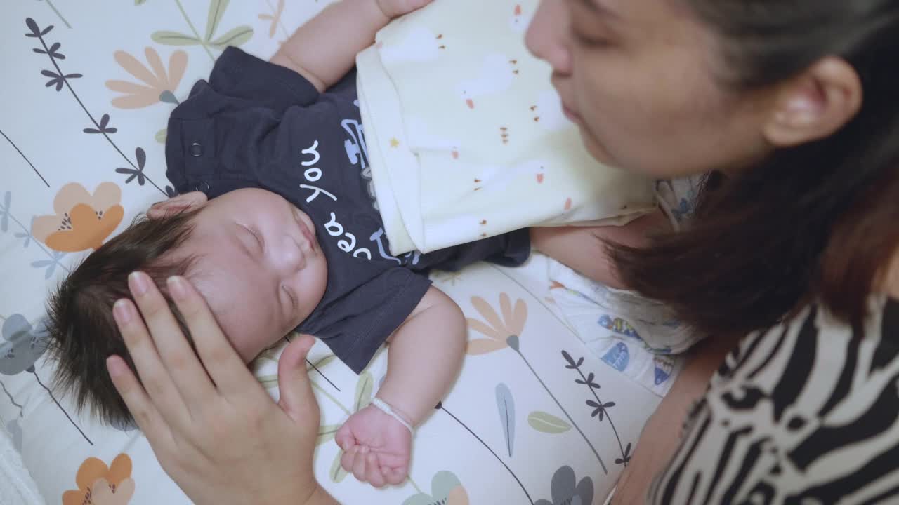 亚洲妈妈轻轻地抚摸她的宝宝，让她在床上睡觉。视频素材