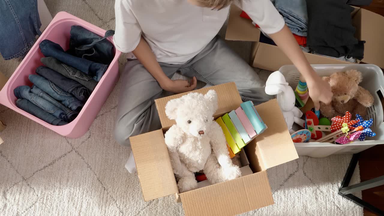 男孩为慈善捐赠准备衣服和玩具。十几岁的男孩把孩子的玩具、衣服放在家里的箱子里。孩子们玩旧玩具，把它们装进纸板箱视频素材