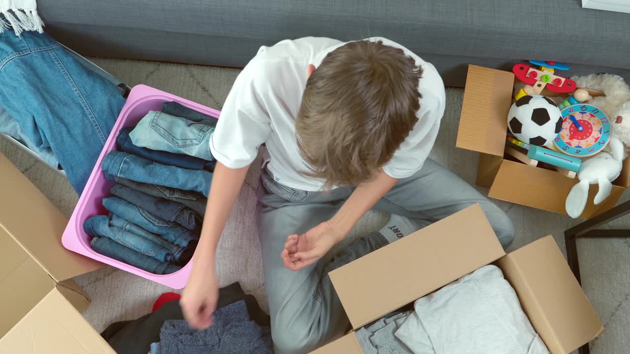 十几岁的男孩折叠和包装衣服纸箱，在家里收集捐赠的东西。为慈善机构捐款，帮助穷人，低收入家庭，移民，难民。俯视图视频下载