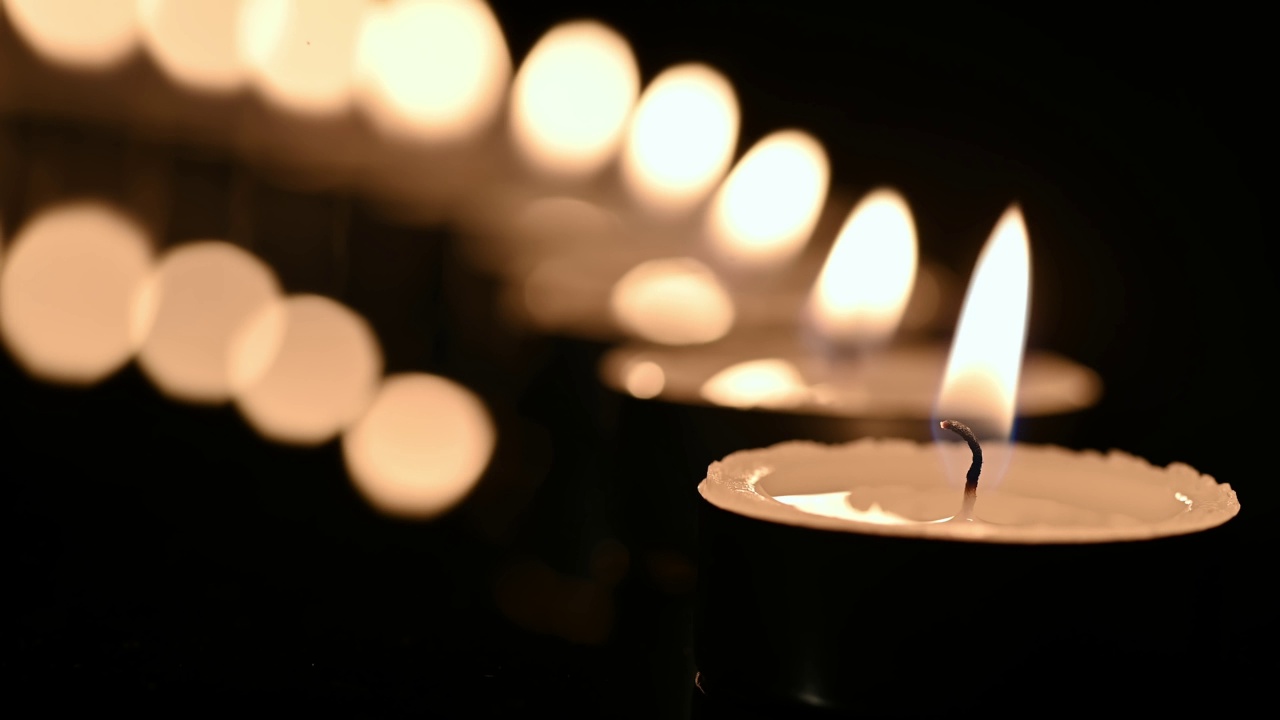 一排燃烧的蜡烛在黑暗的镜子表面。黑色背景视频下载