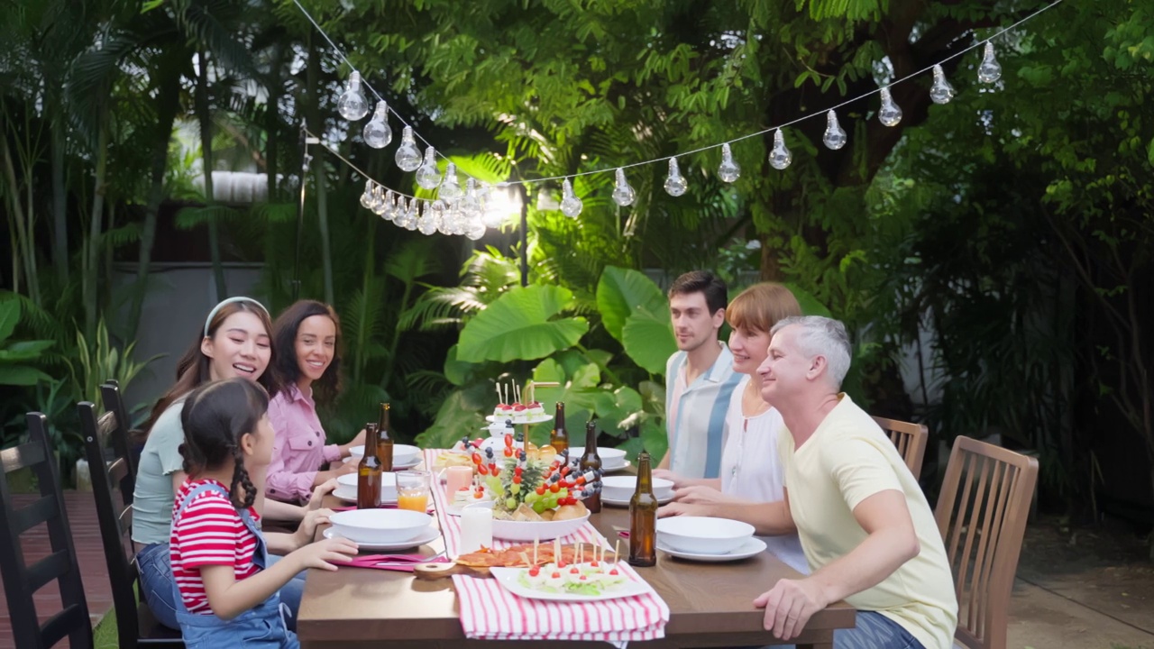 多民族大家庭在户外花园欢聚。各式各样诱人的人聚在一起聚餐，吃着美食，欢度周末团聚。视频素材