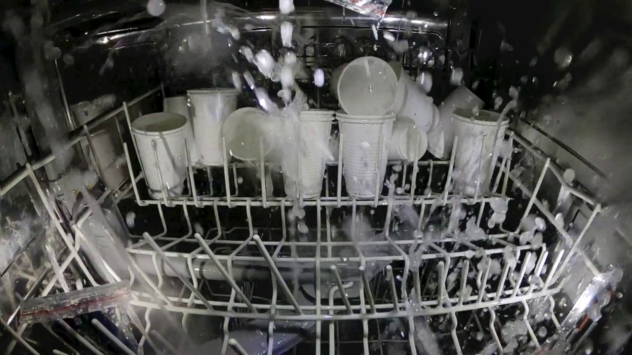 塑料盘子放在洗碗机里洗。疯狂的想法是在洗碗机里洗塑料杯子。查看里面的洗碗机和塑料一次性餐具。慢动作内景。视频下载