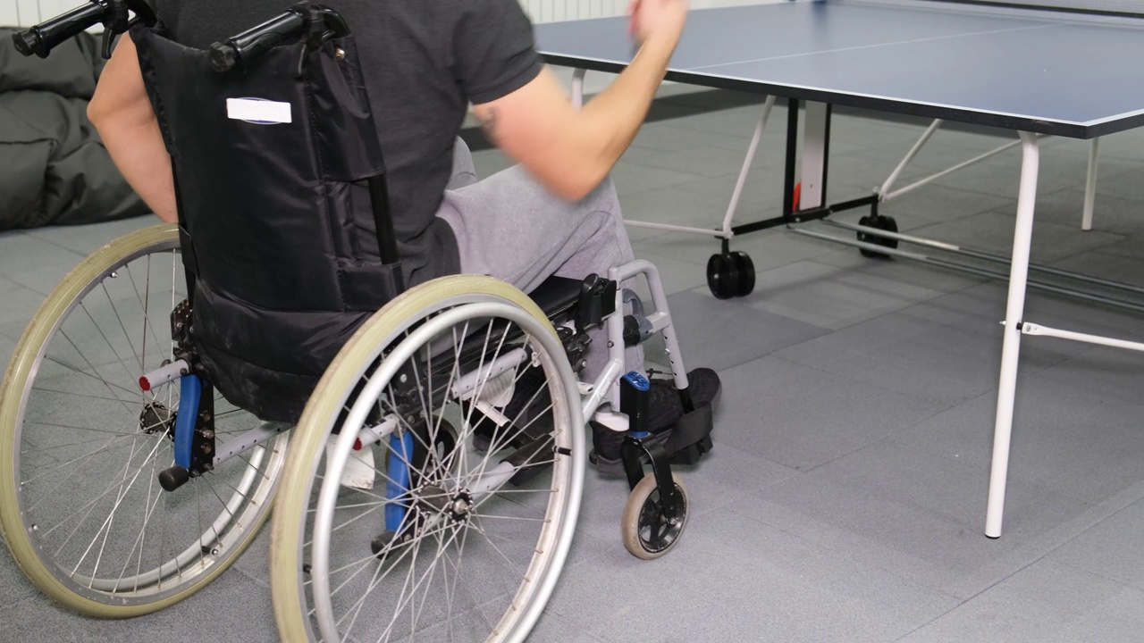 一个坐轮椅的男孩在打乒乓球。残疾人体育运动。视频下载