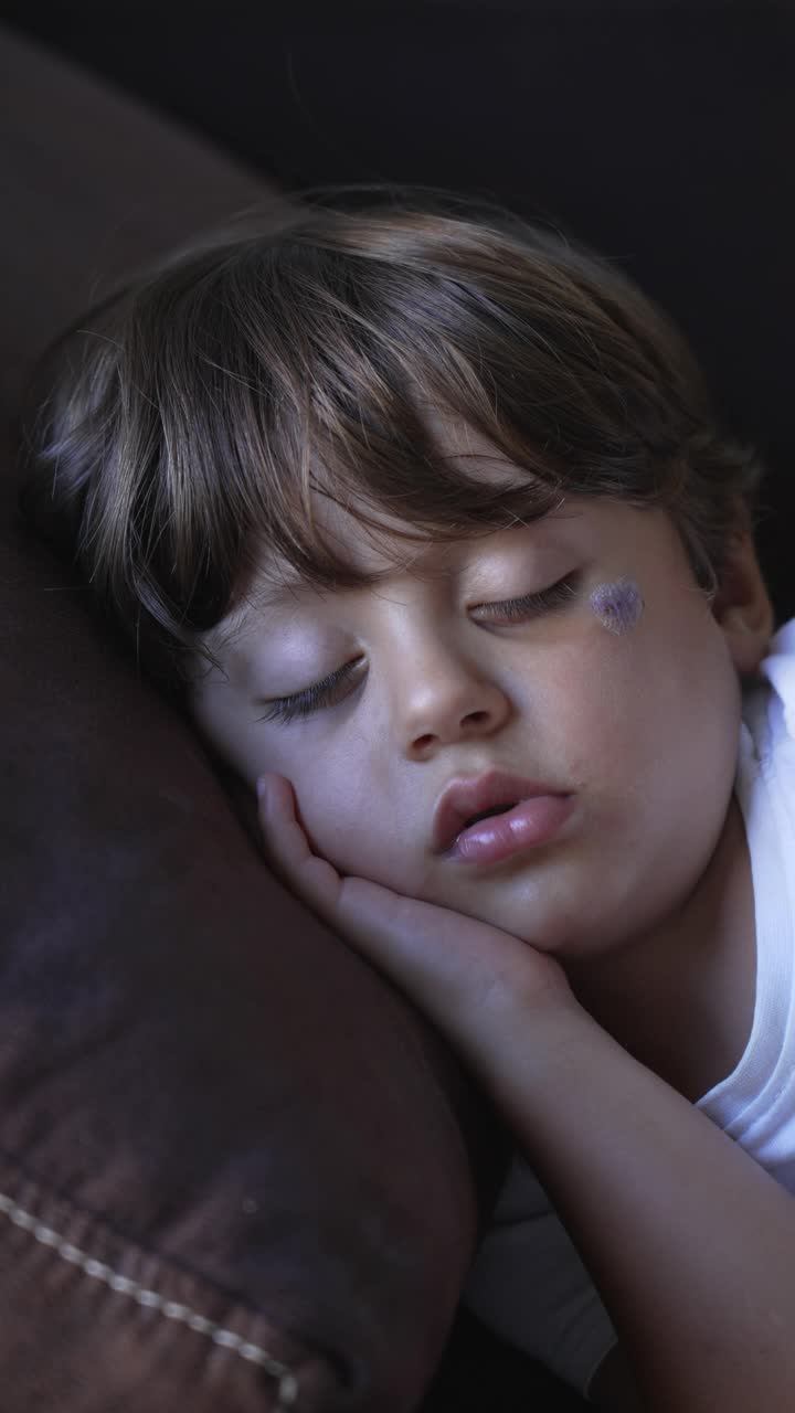 一个小男孩睡在沙发上。在垂直视频中，孩子在沙发上打盹，肖像脸靠近视频素材