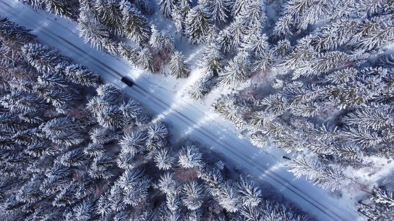 冬季山路上行驶的汽车。鸟瞰白雪皑皑的森林与道路。视频素材