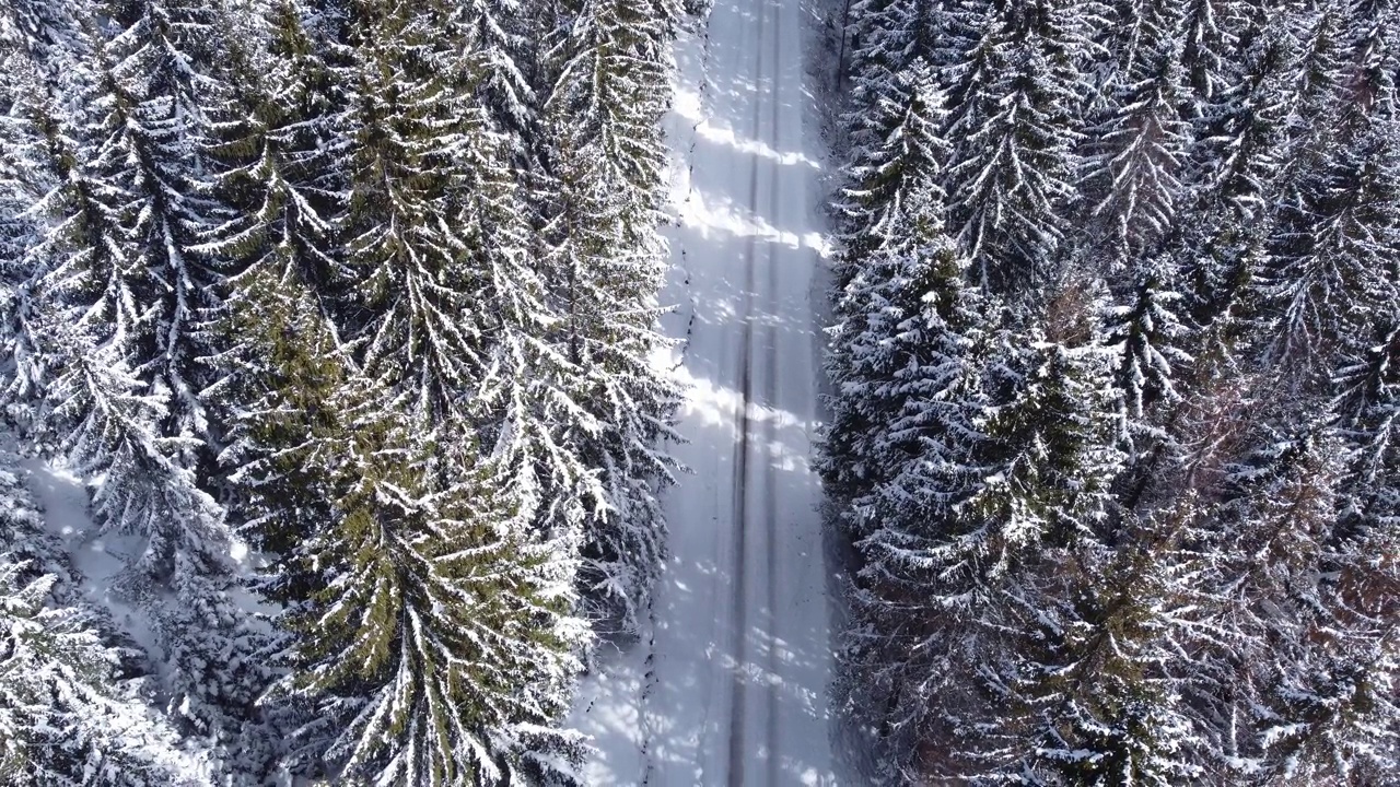冬季山路上行驶的汽车。鸟瞰白雪皑皑的森林与道路。视频素材