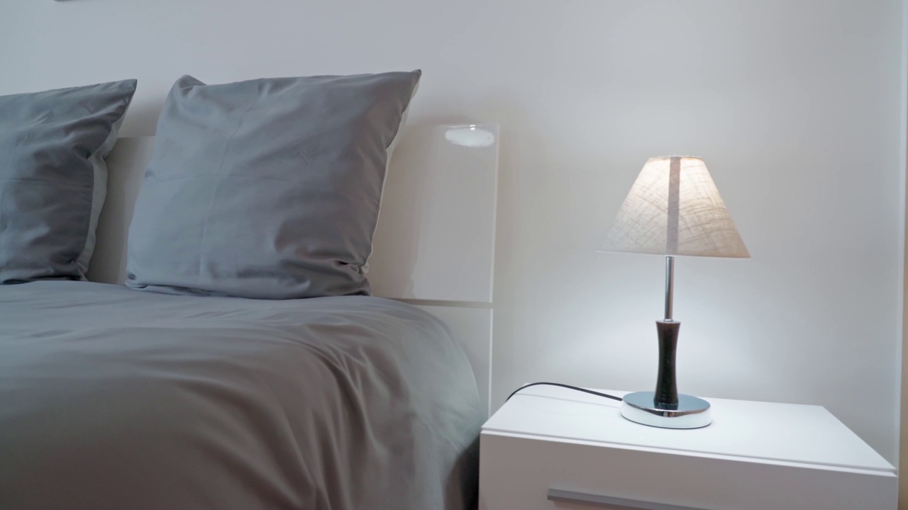 现代极简主义卧室放松和睡眠。床头柜上放着简约的台灯，放着灰色的枕头。视频素材