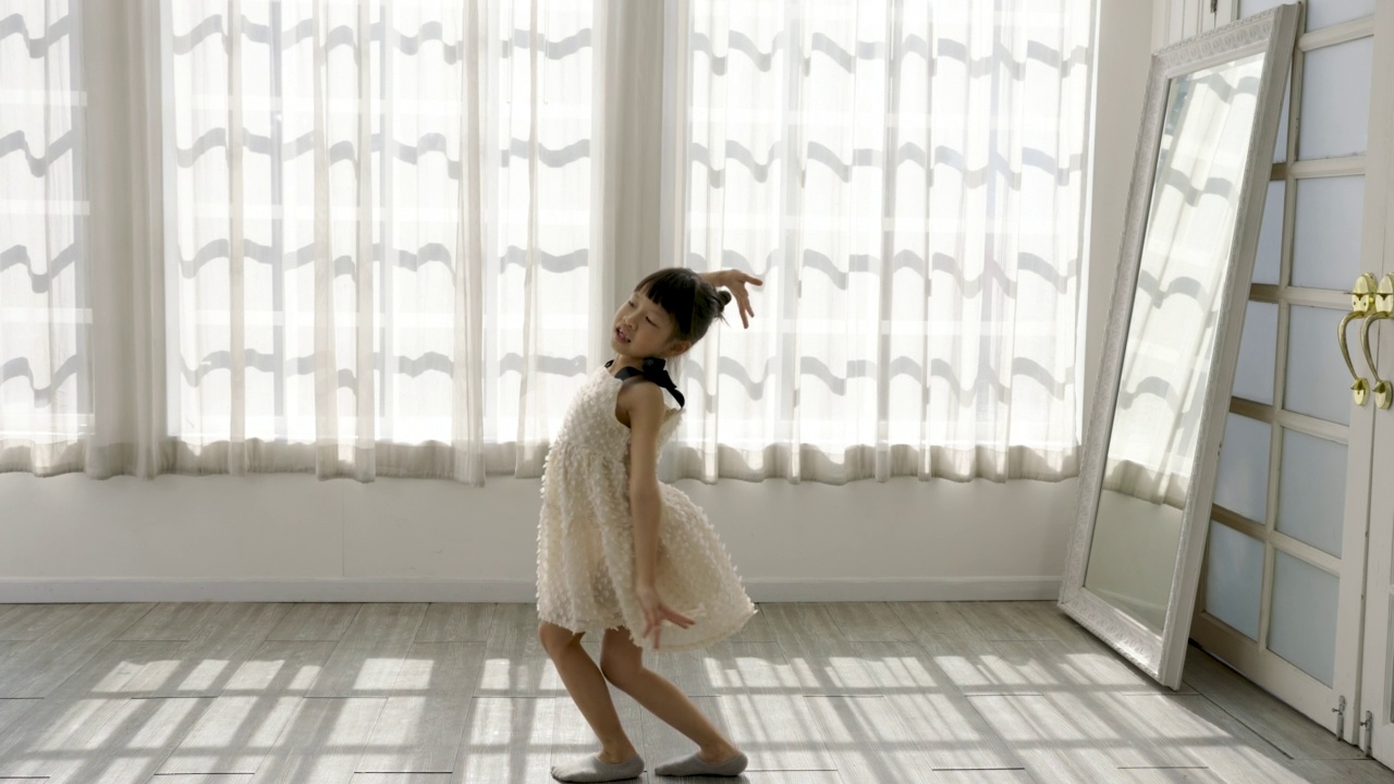 在晨光白色的工作室里，小亚洲女孩梦想成为芭蕾舞演员，穿着粉红色的芭蕾舞裙。快乐的年轻女孩练习她的舞蹈。教育幼儿的生活方式理念视频下载