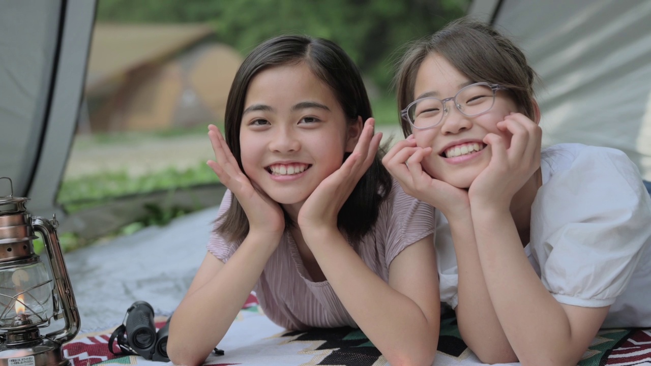 两个十几岁的女孩微笑着躺在帐篷里。视频下载