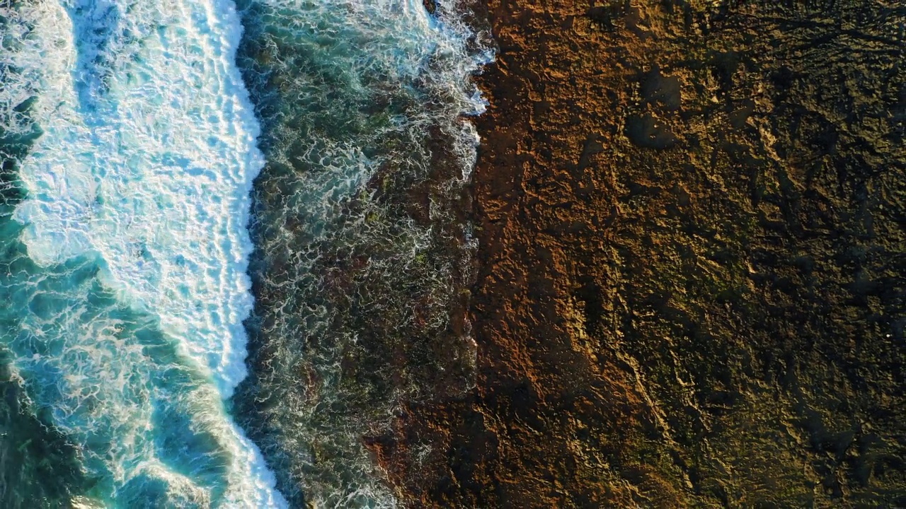 自上而下抽象鸟瞰图的海浪泡沫碰撞岩石海岸线。火山海滩。无人机飞行镜头。视频下载