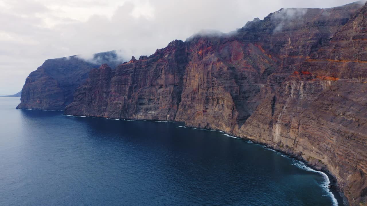 空中飞行在巨大的岩石悬崖和深深蓝色的海洋洛斯吉甘特特内里费。壮观的宁静的大西洋水域。天堂加那利岛之旅。夜间自然与景观。视频素材