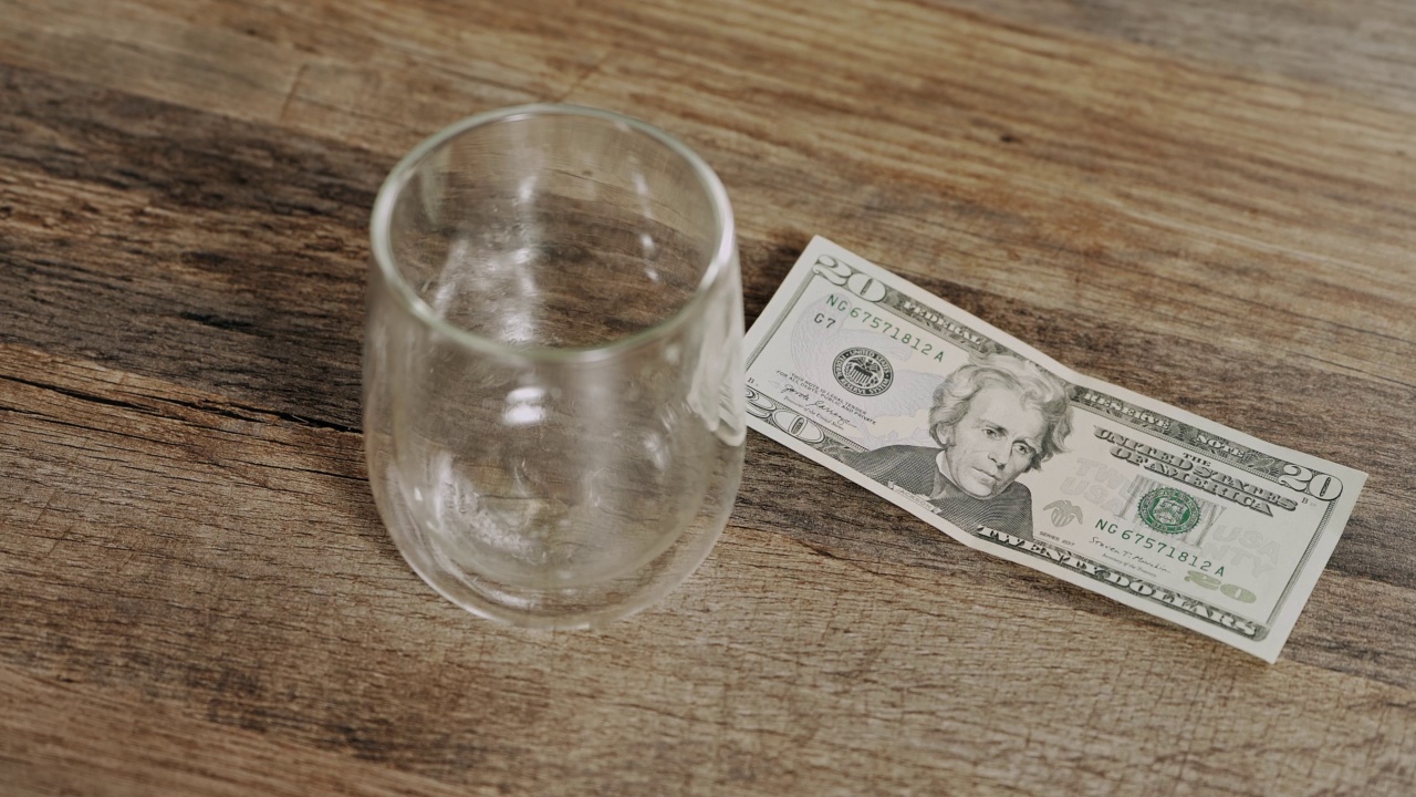 一个男人把一张20美元的钞票放在吧台上一个空酒杯旁边。奖励。休闲、放松、夜店概念。兑换美元。视频下载
