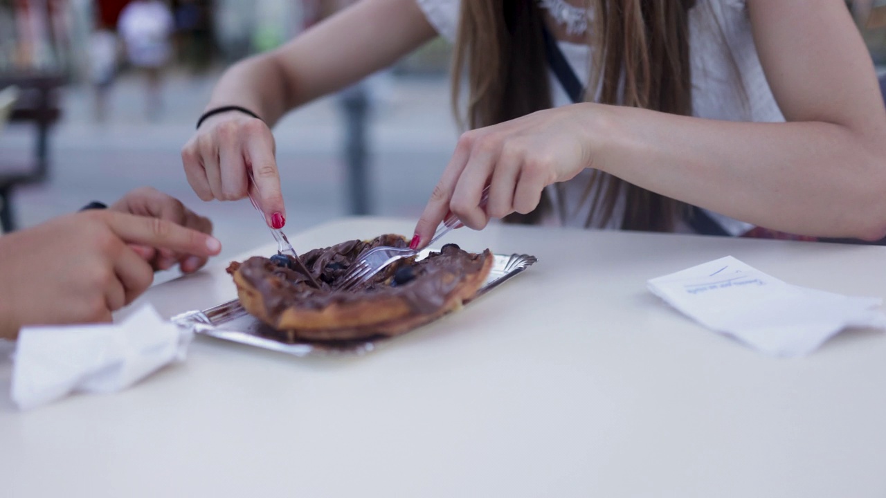 Closeup of teenagers eating a waffle dessert in a sidewalk café.视频下载