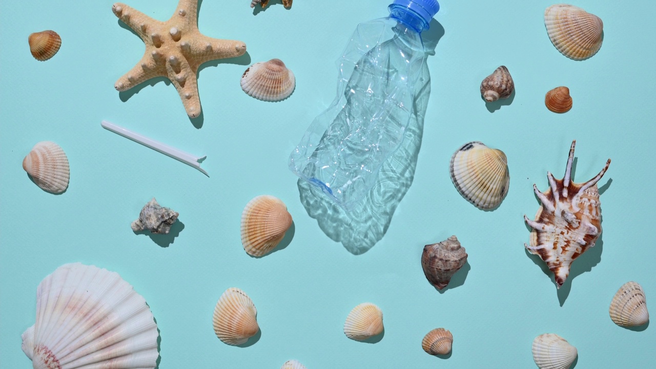 蓝色背景上有许多不同的贝壳和塑料垃圾。塑料污染海洋的概念。视频素材