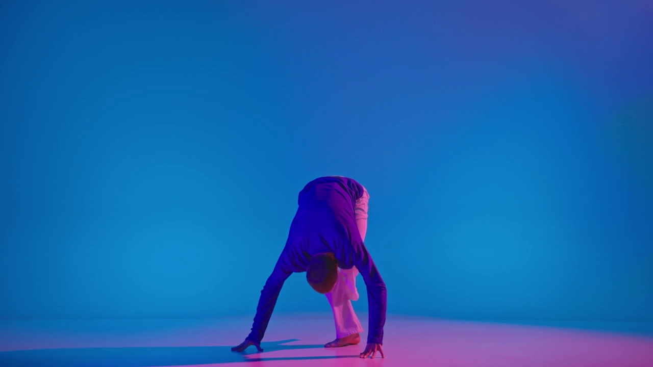 年轻灵活的精力充沛的男子在霓虹灯舞厅的蓝色背景上穿着明亮的运动服跳舞。青春，音乐，风采视频下载