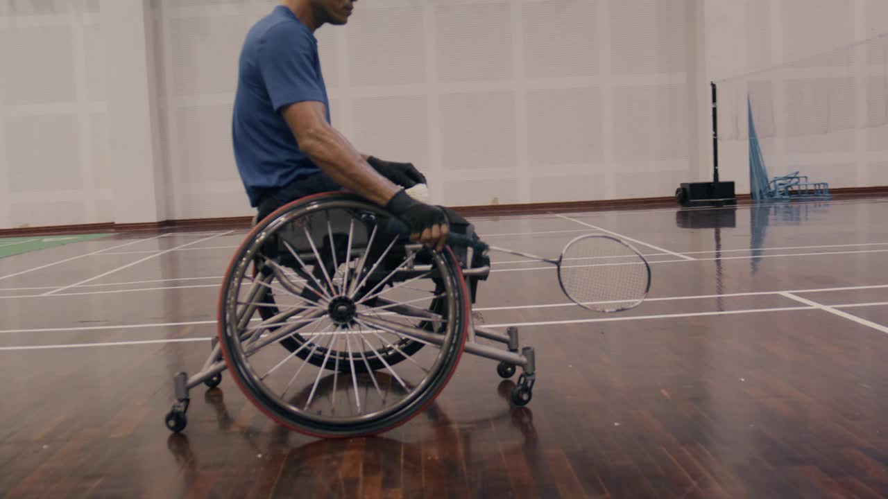 身穿蓝色运动服的残疾亚裔男子坐在竞技轮椅上，手里拿着羽毛球拍。视频下载