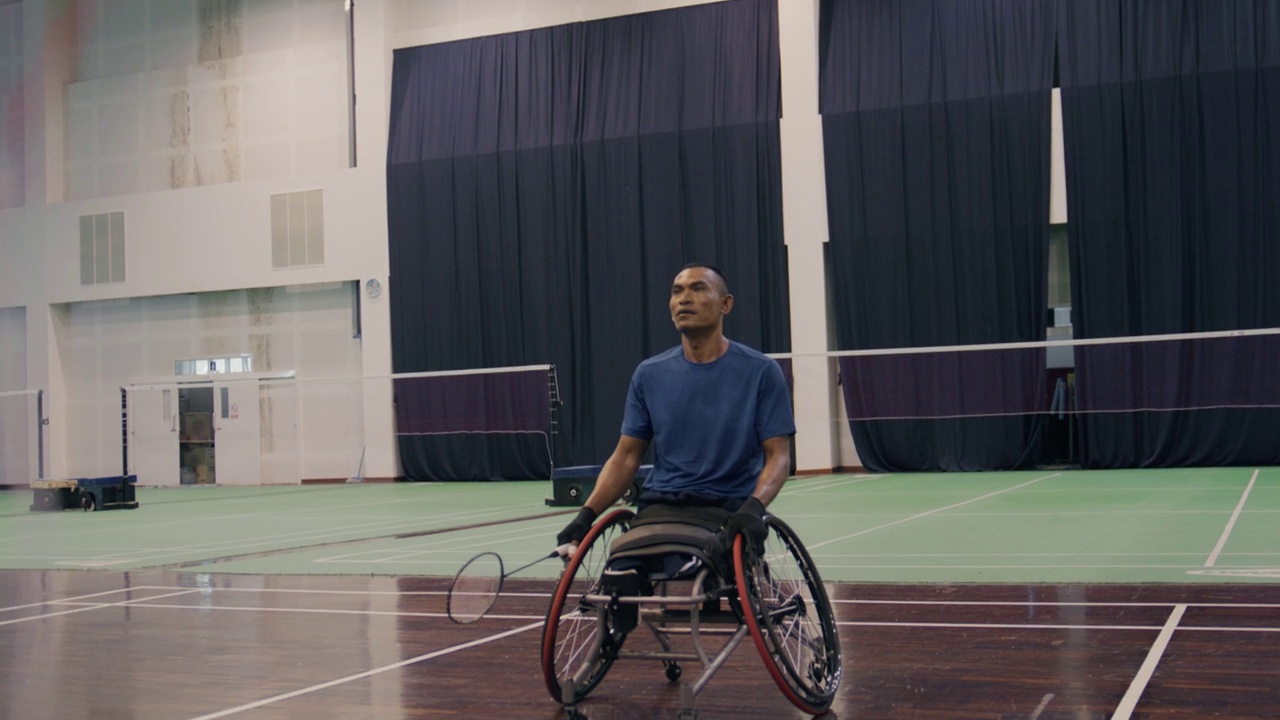 身穿蓝色运动服的残疾亚裔男子坐在竞技轮椅上享受比赛视频下载