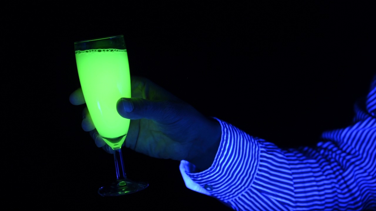 一个人在迪斯科舞厅用酒精饮料欢呼的特写。紫外线灯光。视频下载