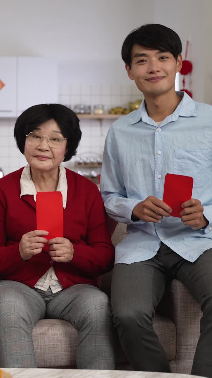 竖屏:儿子和奶奶用拇指和胜利的手势对着镜头微笑，在中国农历新年拿着压岁钱拍爆照。翻译:幸运视频下载