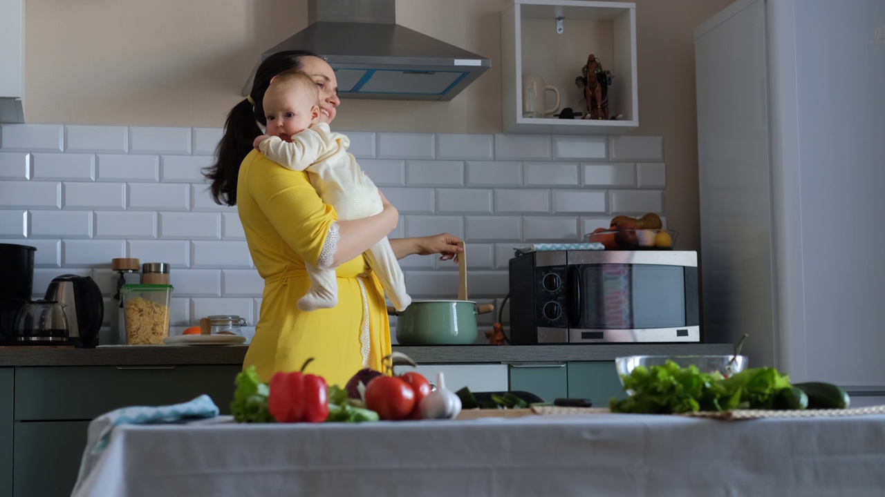年轻女子抱着婴儿在厨房做饭视频下载