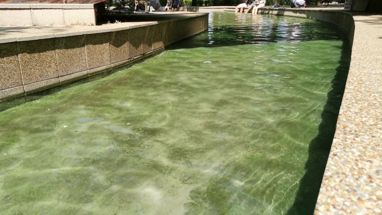 温泉公园里的暖流。河床用石板装饰，底部有绿藻。远处的人把脚搁在小溪里。尼斯卡·巴尼亚，塞尔维亚视频下载
