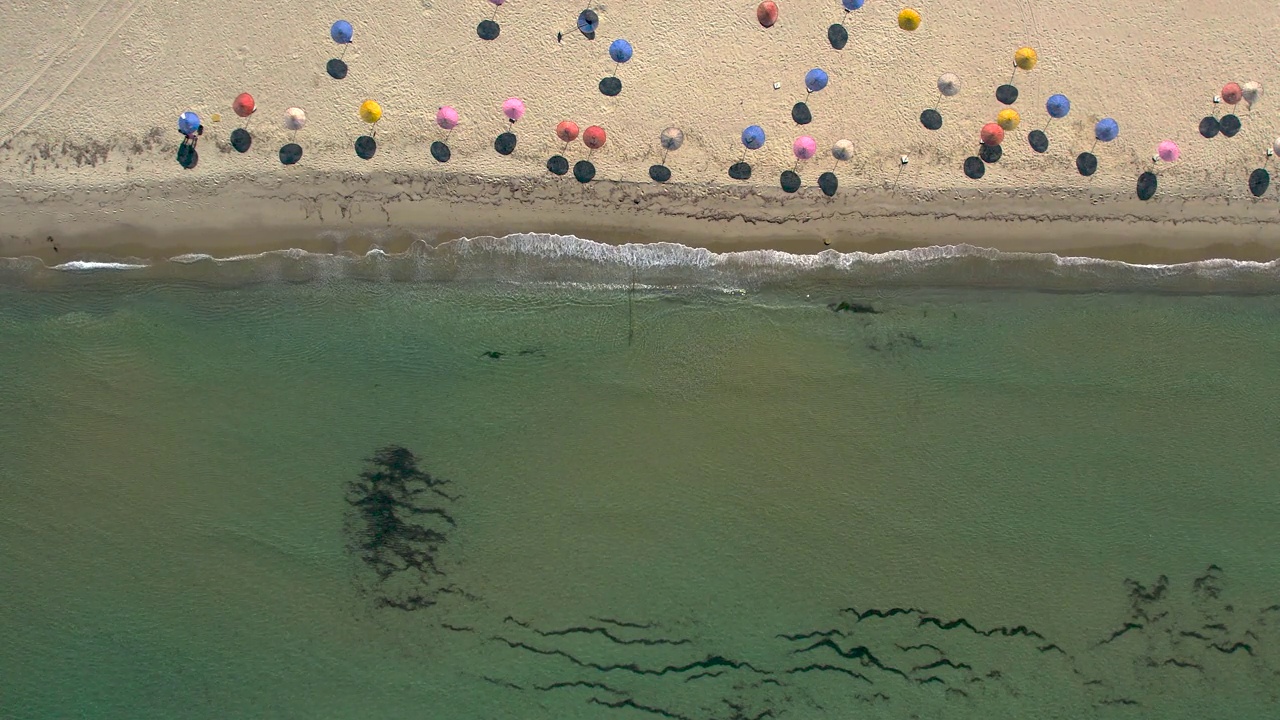绿色海浪的鸟瞰图和彩色雨伞的海滩。视频下载