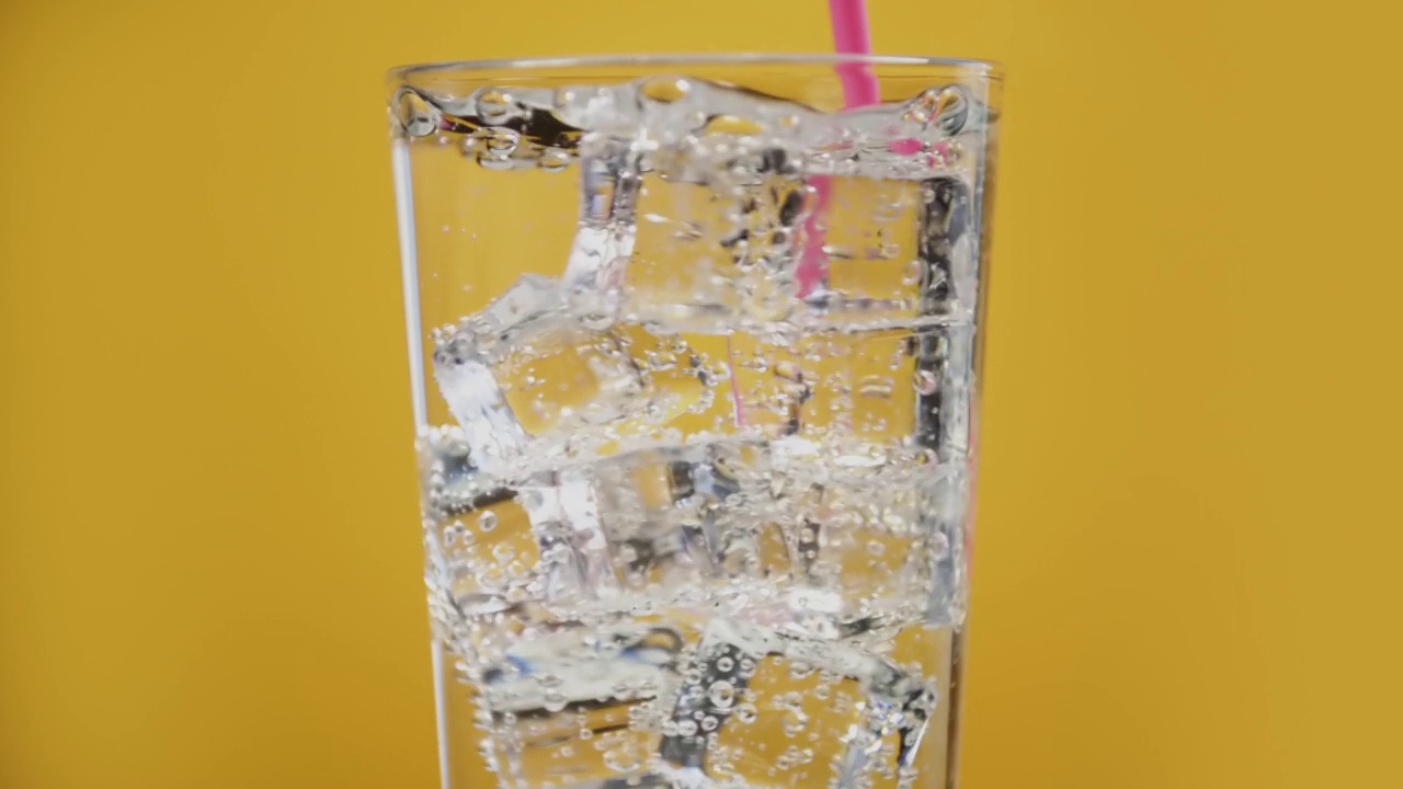 有人用粉红色的吸管混合凉水饮料。杯子里装满了气泡和冰块视频素材