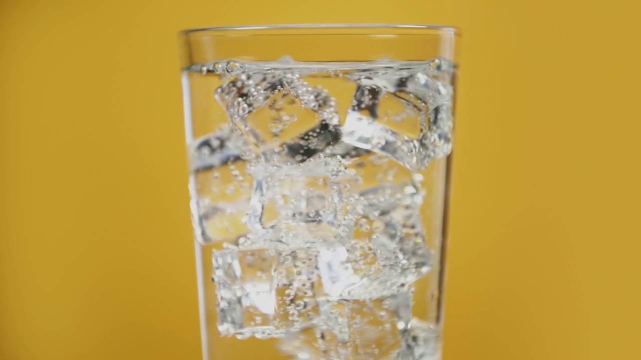 透明碳酸饮料。杯子里装满了冰凉的气泡水，黄色背景上有冰块视频素材